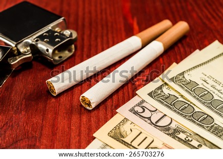 Couple of cigarettes with brown filters and a several dollar bills with lighter on the table. Focus on the cigarettes