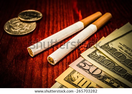Couple of cigarettes with brown filters and a several dollar bills with coins on the table. Focus on the cigarettes, image vignetting