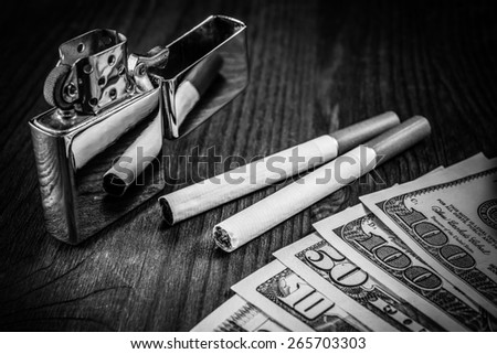 Couple of cigarettes with brown filters and a several dollar bills with lighter on the table. Focus on the cigarettes, image vignetting and black and white tones