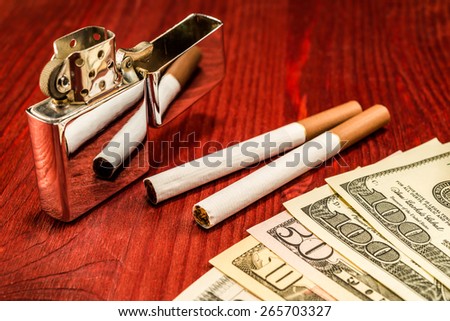 Couple of cigarettes with brown filters and a several dollar bills with lighter on the table. Focus on the cigarettes