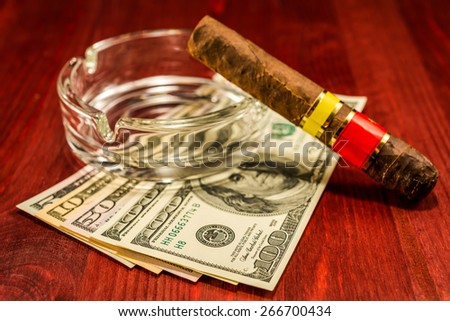Cuban cigar with glass ashtray on a several dollar bills on the table. Focus on the dollars