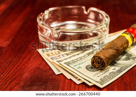 Cuban cigar with glass ashtray on a several dollar bills on the table
