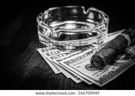 Cuban cigar with glass ashtray on a several dollar bills on the table. Image vignetting and black and white tones