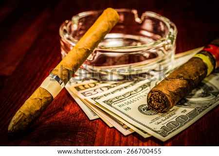 Two cuban cigars with glass ashtray on a several dollar bills on the table. Image vignetting