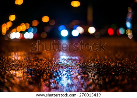 Night city after rain, car goes on the road. View from the level of asphalt