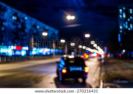 Night city after rain, car goes on the road. Defocused image, in blue tones