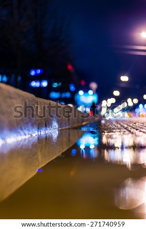Night city after rain, a reflection of the city at night in the water. View of the stream of cars from the roadside at the asphalt level, in blue tones