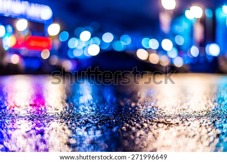 Shop windows are reflected on the wet asphalt after rain. View from the level of asphalt, in blue tones