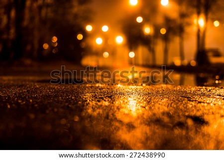 Night city alley with lanterns in the fog after rain. View from the level of asphalt, in yellow tones