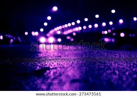 City night lights, road bridge with the lights and moving cars in the fog after rain. View from the level of asphalt, image in the purple-blue toning