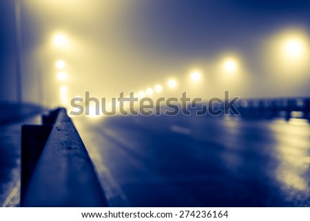 The bright lights of the city at night, the headlights of the approaching cars on the road bridge. View of the highway with a dividing border, image in the yellow-blue toning