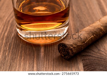 Glass of whiskey and cuban cigar on a wooden table. Focus on the cuban cigar