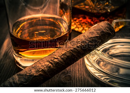 Decanter of whiskey and a glass with cuban cigar on a wooden table. Image vignetting and the orange-blue toning