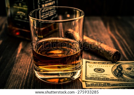 Bottle of whiskey and a glass with cuban cigar and money on a wooden table. Image vignetting and the orange-blue toning