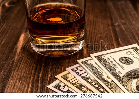 Glass of whiskey with money on a wooden table. Close up view, focus on the money