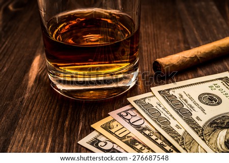 Glass of whiskey and a money with cuban cigar on a wooden table. Close up view, focus on the money