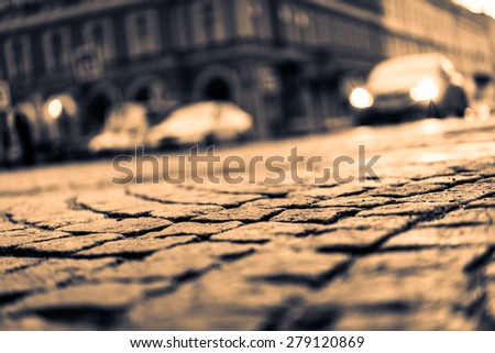 City street paved with stone, glowing lights of the approaching car. View from the pavement level, image in the yellow toning