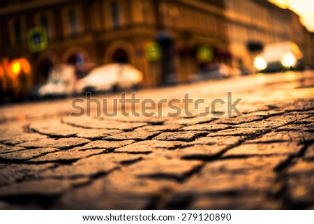 City street paved with stone, glowing lights of the approaching car. View from the pavement level, image vignetting and the yellow toning