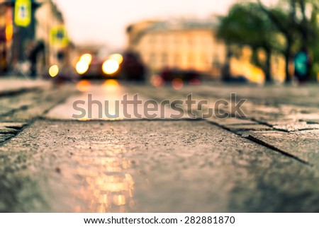 City central square paved with stone after a rain, headlights from car in the distance. View from the pavement level, image in the yellow toning