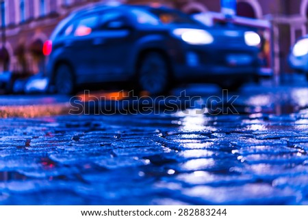 The bright lights of the evening city, driving car. View from the pavement level, image in the blue toning