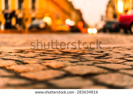 City street paved with stone, on which riding cars. View from the pavement level, image in the orange-yellow toning
