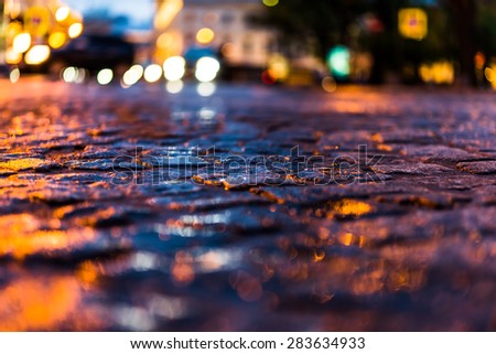 The bright lights of the evening city after rain, headlights from cars in the distance. View from the pavement level
