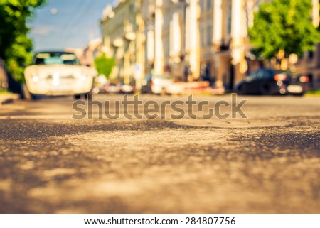 City on a sunny day, a quiet street after rain with trees and cars. View from the level of asphalt, image in the yellow-blue toning