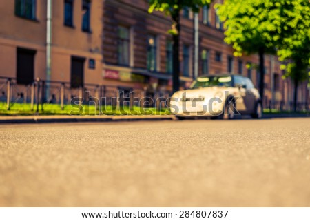 City on a sunny day, a quiet street with trees and parking car. View from the level of asphalt, image in the yellow-blue toning