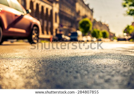 City on a sunny day, a quiet city street after rain on which passing car. View from the level of asphalt, image in the yellow-blue toning