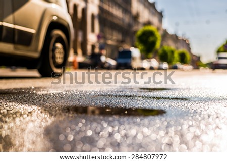 City on a sunny day, a quiet city street after rain on which passing car. View from the level of asphalt