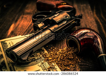 Money and a gun with a pipe on a wooden table. Image vignetting and the orange-blue toning