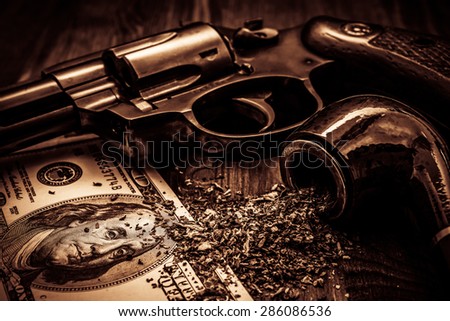 Money and a gun with a pipe on a wooden table. Image vignetting and the yellow-orange toning