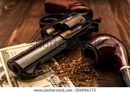 Money and a gun with a pipe on a wooden table