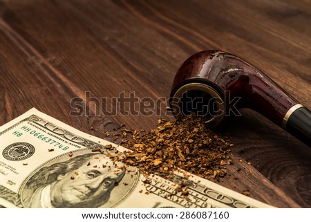 Tube for smoking tobacco and money on a wooden table
