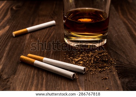 Glass of whiskey and three cigarettes with tobacco leaves on a wooden table. Focus on the tobacco