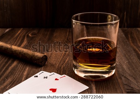 Glass of whiskey and playing cards with cuban cigar on the wooden table. Angle view, identification cards ace Russian letter