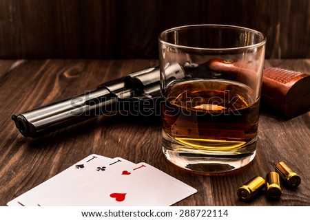 Glass of whiskey and playing cards with revolver on the wooden table. Angle view, identification cards ace Russian letter
