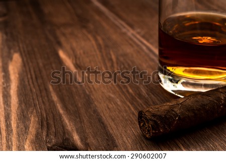 Glass of whiskey and cuban cigar on a wooden table. Close up view, focus on the cuban cigar