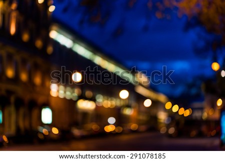 The bright lights of the evening city, empty city street with trees. Defocused image