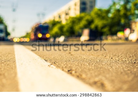 Sunny day in a city, tram rides on rails next to the stream of cars, the view from the level of asphalt. Image in the yellow-blue toning