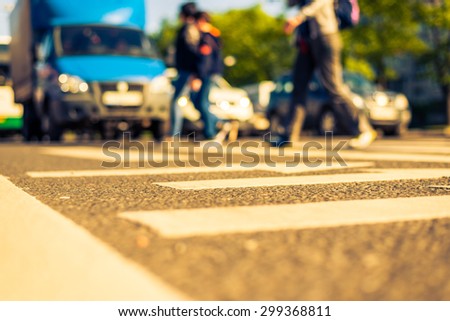 Sunny day in a city, pedestrians crossing the road. View from the level of asphalt, image in the yellow-blue toning