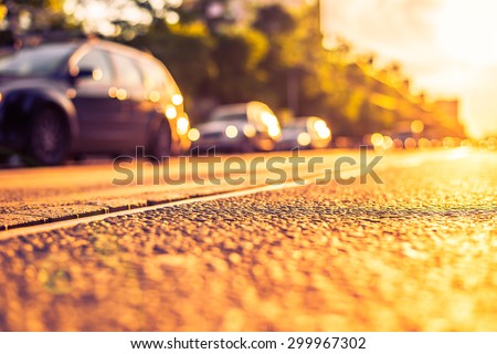Sunny day in a city, view of the driving cars from the level of the tram rails. Image in the orange-purple toning