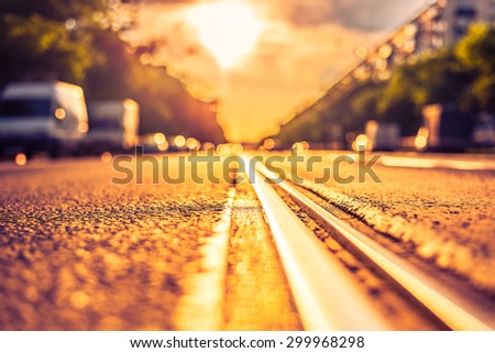 Sunny day in a city, view of the headlights of approaching cars from the level of the tram rails. Image in the orange-purple toning