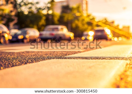 Sunny day in a city, view of the passing cars with level pedestrian crossing. Image in the orange-purple toning