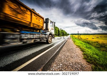 Truck driving on a rural road. View from the side of the road, image vignetting and hard tones