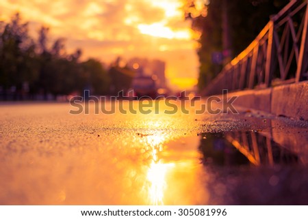 Sun after the rain in the city, view of the cars with a level of puddles on the pavement. Image in the soft orange-purple toning