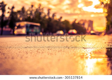 Sun after the rain in the city, view of the bus with a level of puddles on the pavement. Image in the orange-purple toning