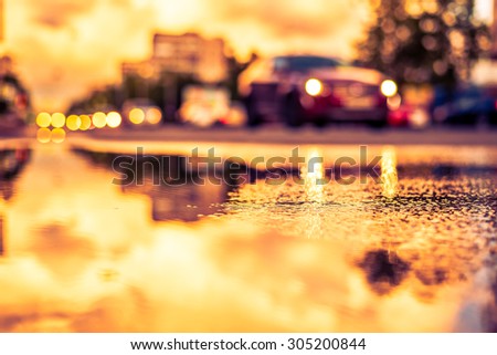 Sun after the rain in the city, view of the approaching car with a level of puddles on the pavement. Image in the yellow-purple toning