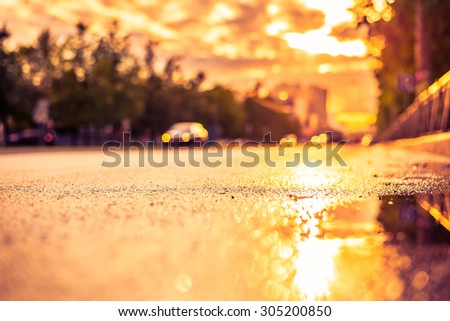 Sun after the rain in the city, view of the car with a level of puddles on the pavement. Image in the yellow-purple toning