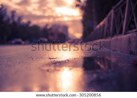 Sun after the rain in the city, view of the cars with a level of puddles on the pavement. Image in the soft orange-purple toning